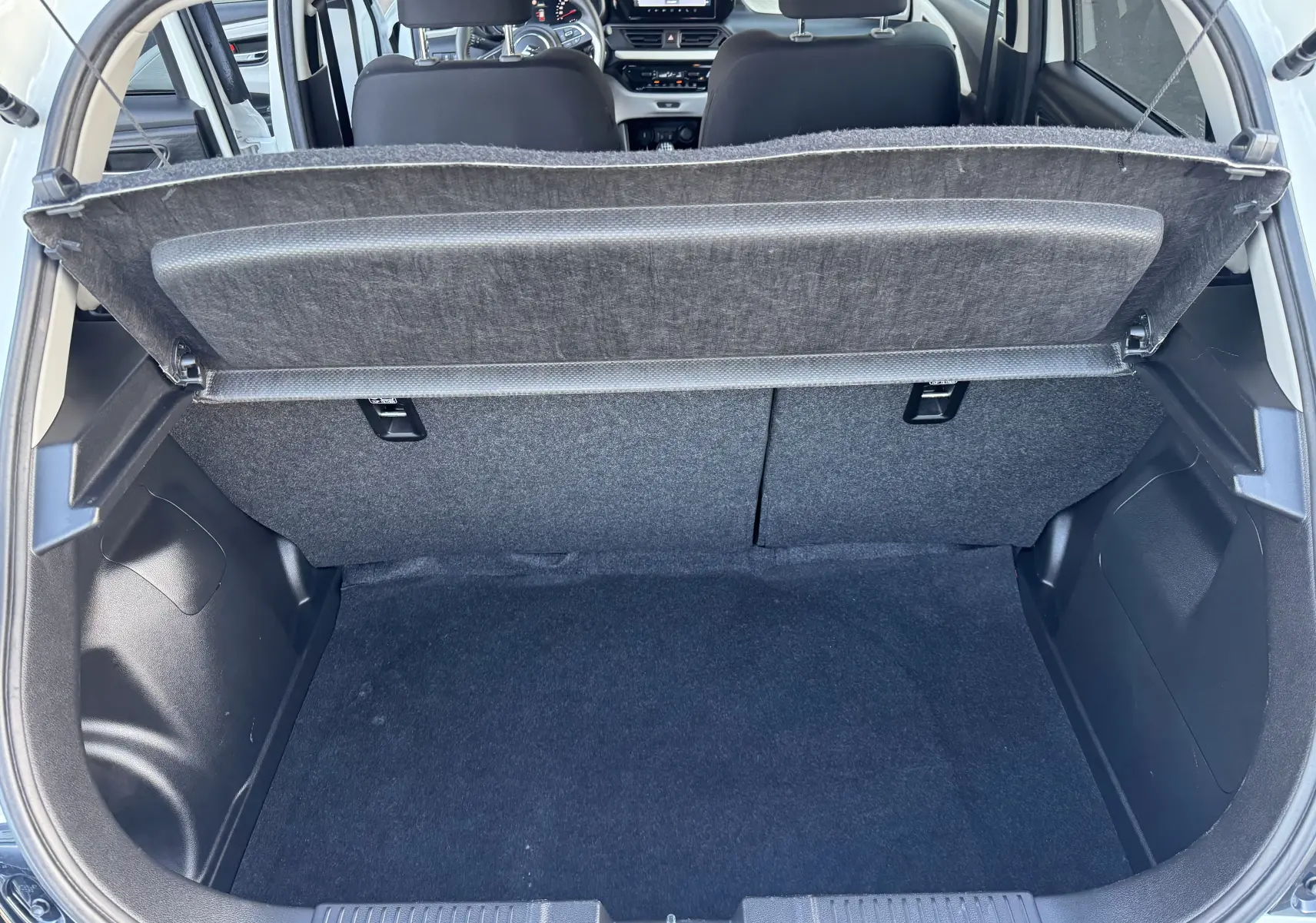 Vue depuis le coffre ouvert d'une Suzuki Swift 1.2 Privilège Hybrid blanche, montrant l'espace de chargement et l'intérieur arrière.