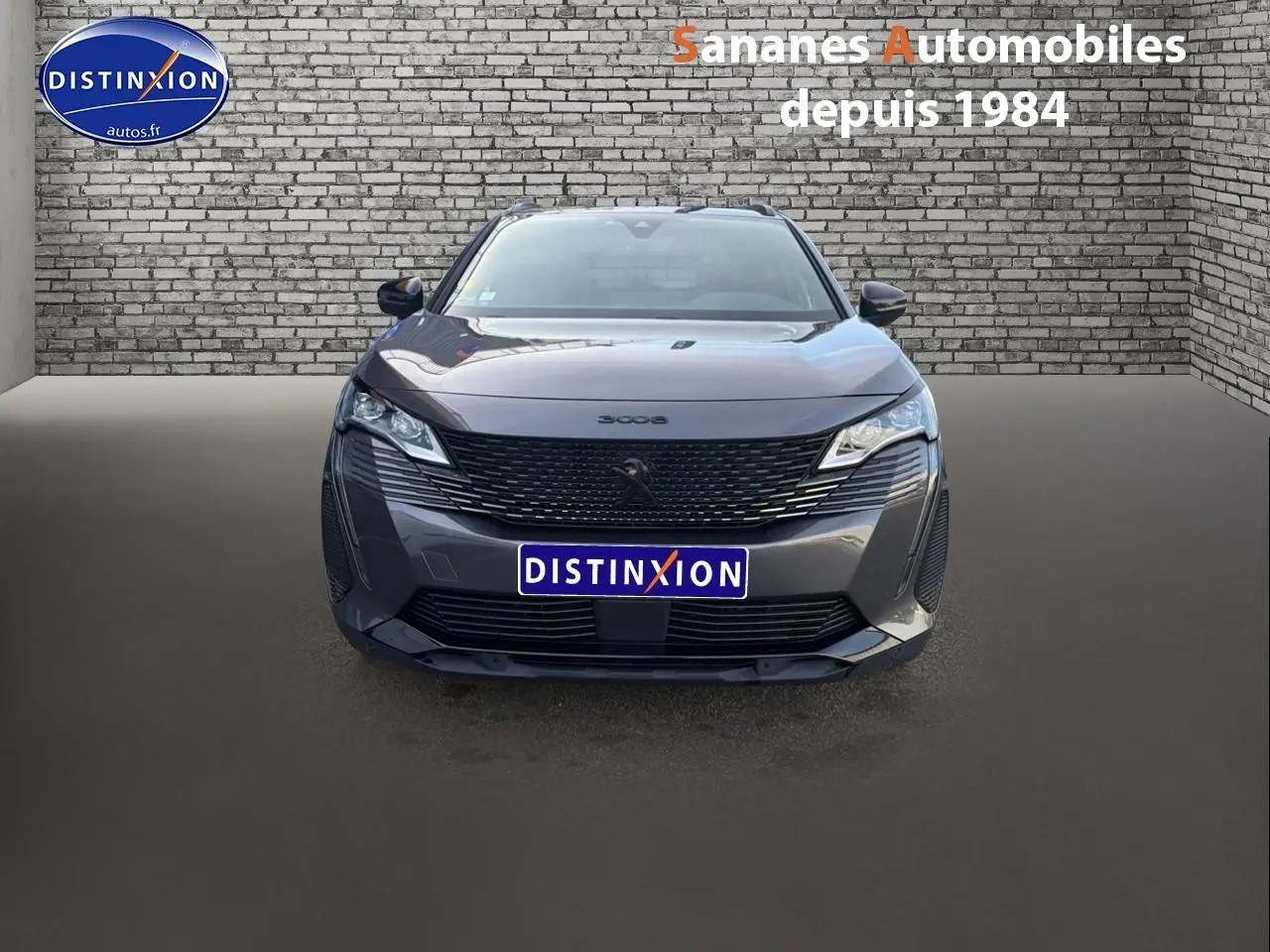 Vue avant d'un Peugeot 3008 gris foncé avec calandre noire et logo lion Dark Chrome sur fond urbain en briques.