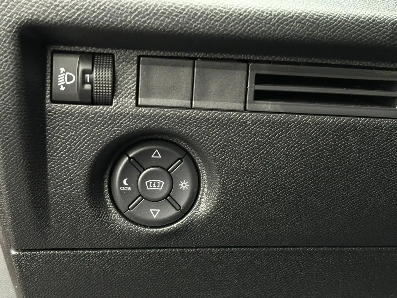 Détail du tableau de bord noir texturé avec commandes de réglage des phares et de l'affichage dans une Citroën C4 Hybrid 2025.