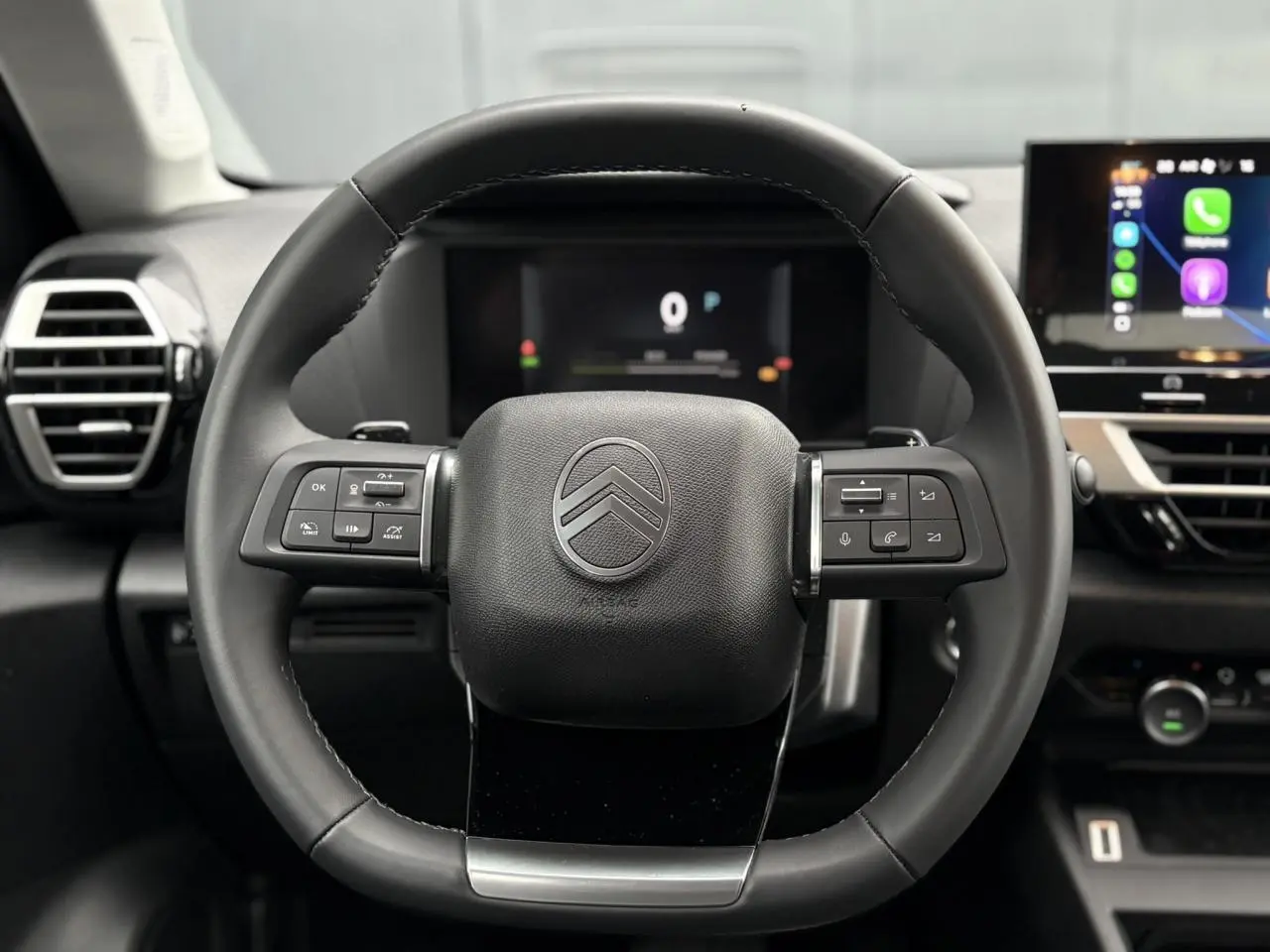 Vue rapprochée du volant cuir noir de la Citroën C4 Hybrid 2025 avec commandes intégrées et tableau de bord numérique.