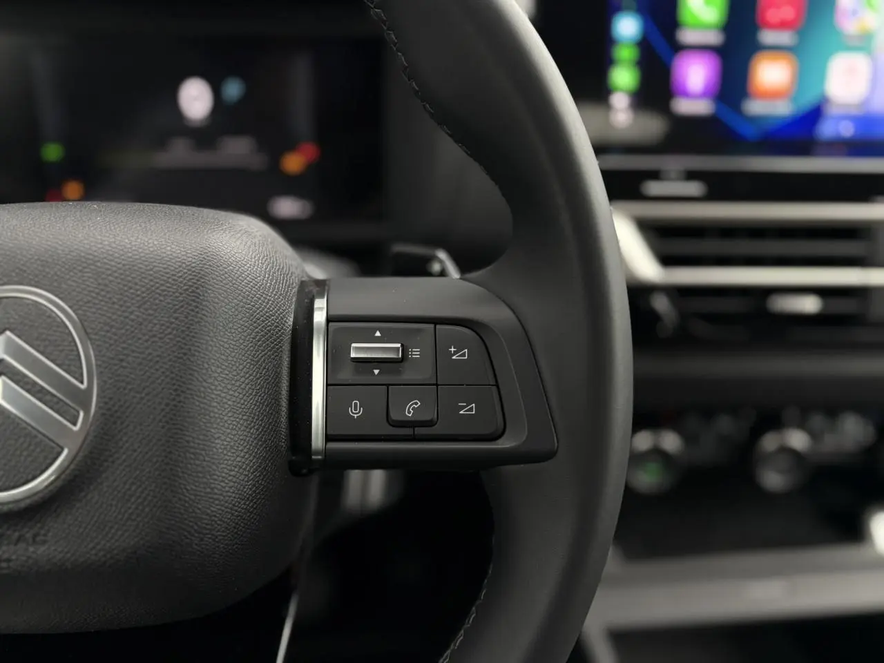 Gros plan sur le volant cuir noir de la Citroën C4 Hybrid 2025 avec commandes vocales et écran tactile flou en arrière-plan.
