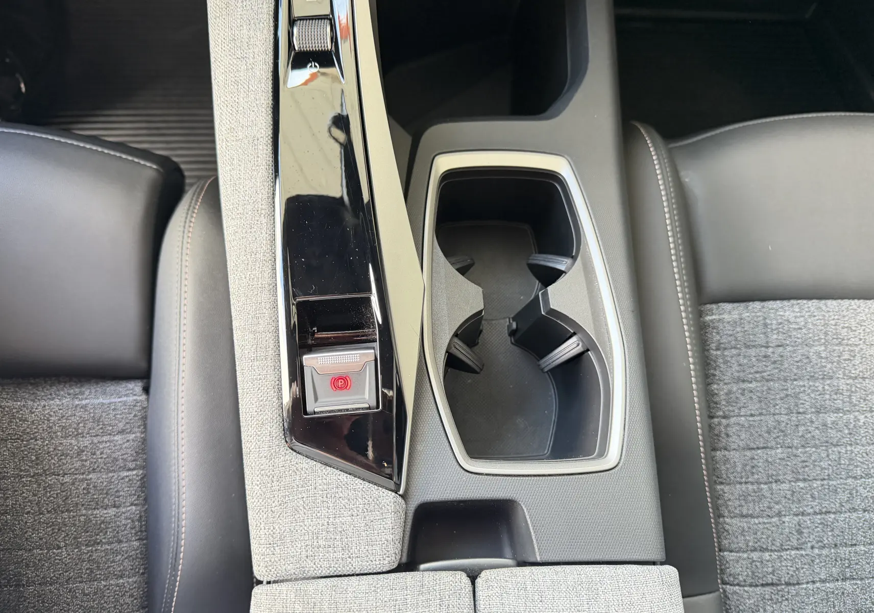 Vue plongeante sur la console centrale grise et noire du Peugeot 1007 Hybrid avec porte-gobelets et bouton frein à main électrique.