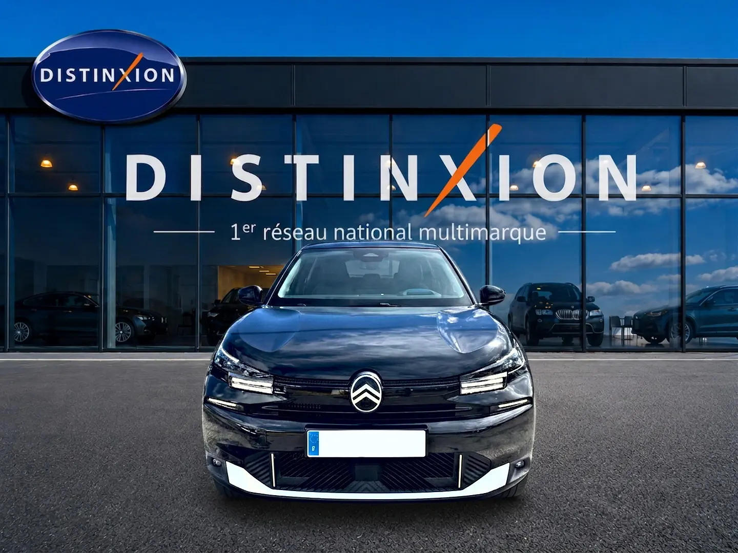 Vue de face d'une Citroën C4 X noire 2025 avec calandre distinctive et phares LED, devant une vitrine Distinxion.