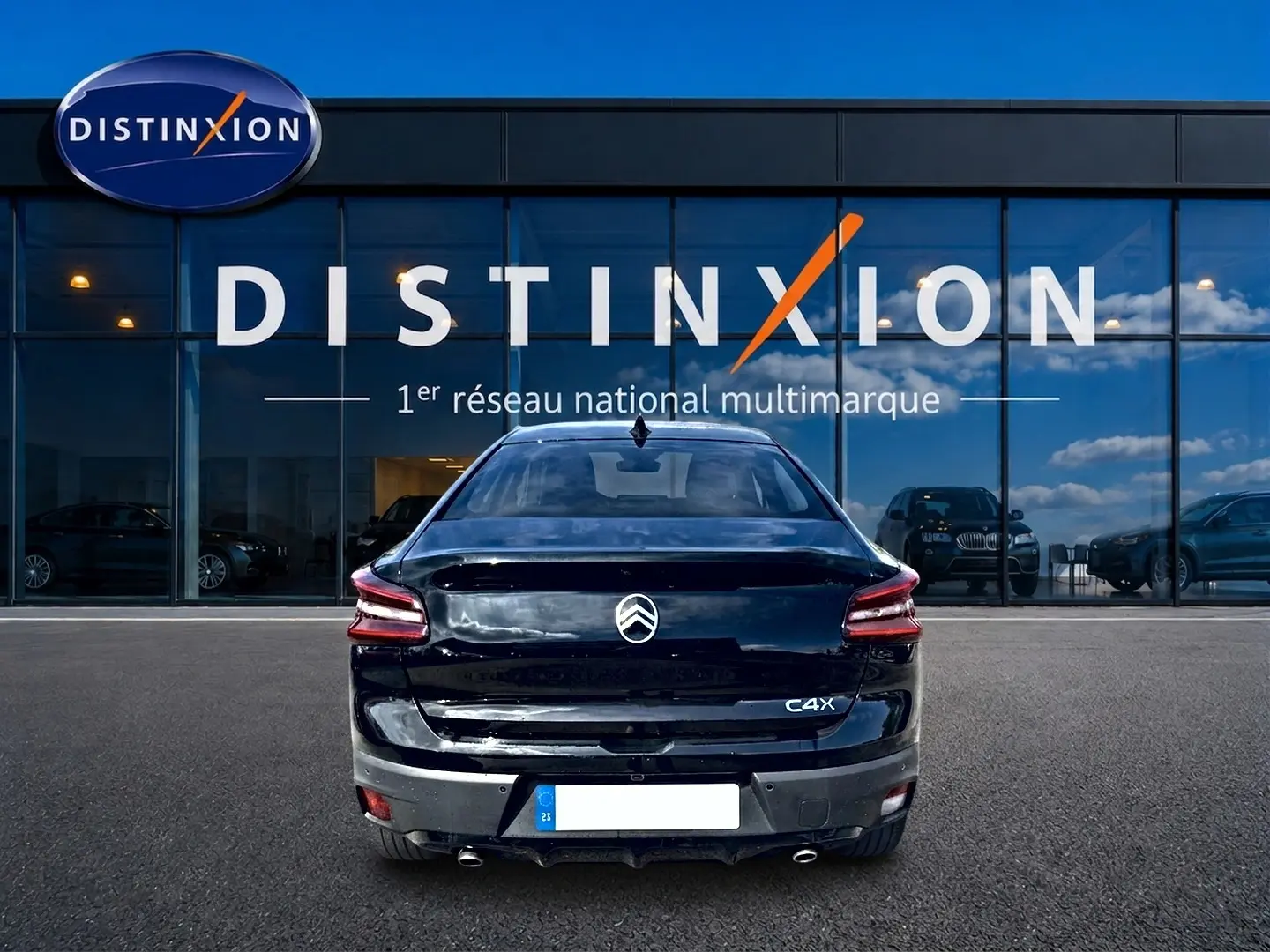 Vue arrière d'une Citroën C4 X noire 2025 avec feux LED et double sortie d'échappement chromée, devant un showroom Distinxion.