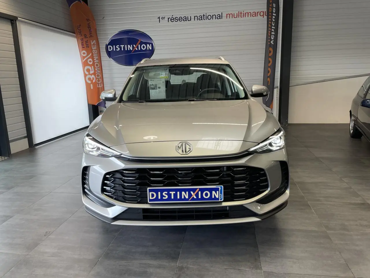 Vue frontale du MG ZS 1.5 Hybrid+ gris clair avec calandre noire et phares LED allumés en showroom.