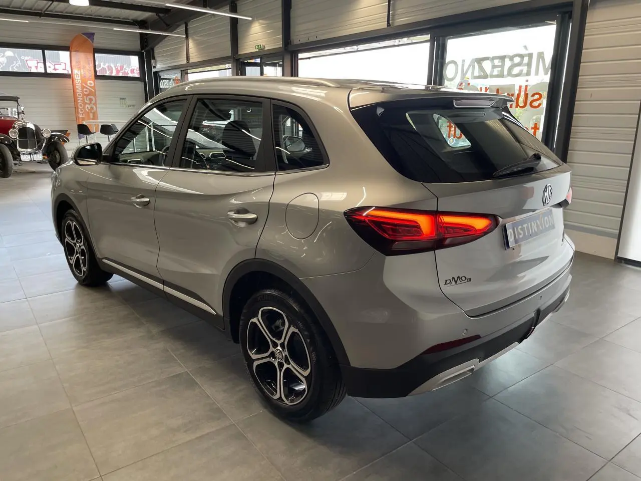 Vue 3/4 arrière droite d’un MG ZS gris clair 2026 avec feux LED allumés et jantes alliage 17 pouces en showroom.