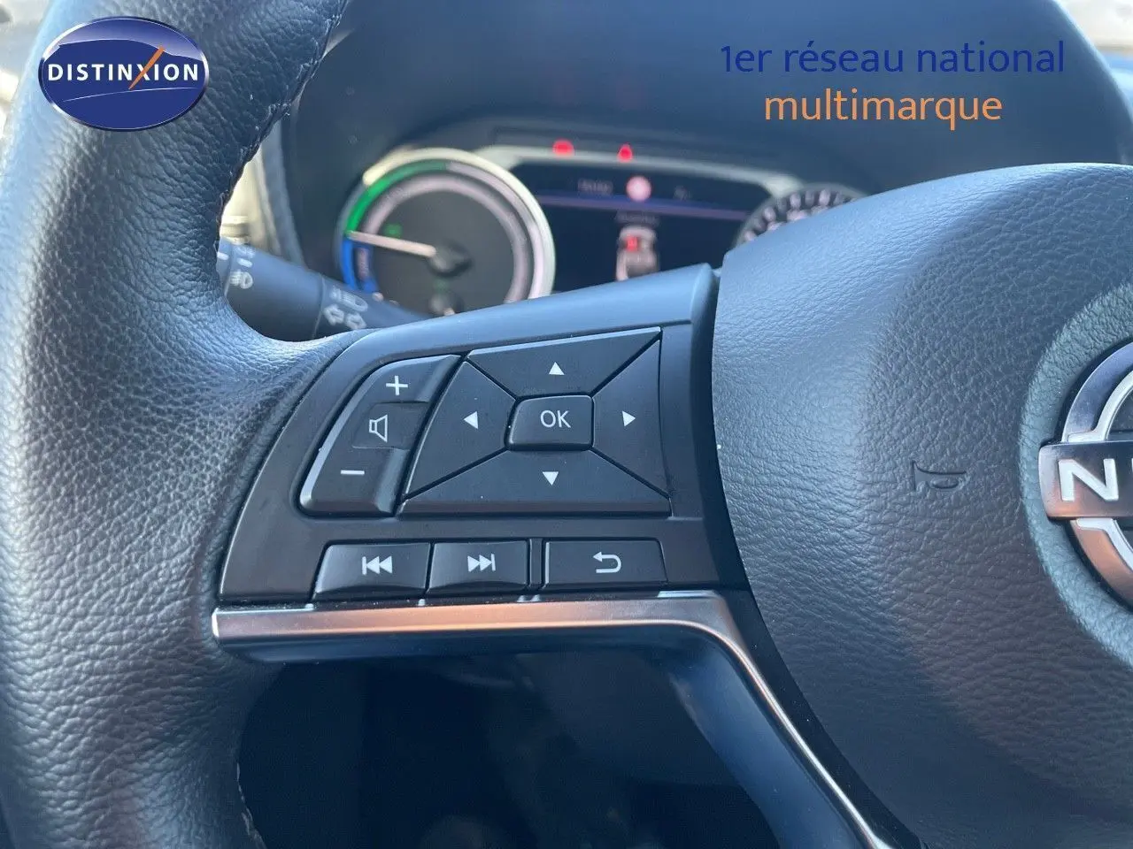 Gros plan sur les commandes au volant d'un Nissan Juke 2024 gris squale métal, avec tableau de bord hybride en arrière-plan.