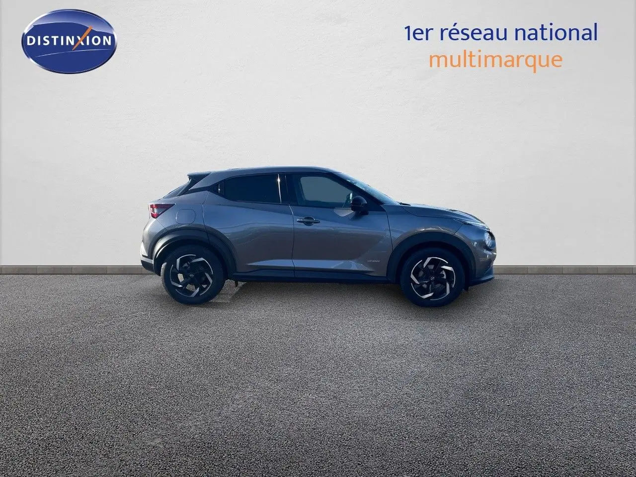 Profil latéral droit d'un Nissan Juke 2024 gris squale métal avec jantes noires et toit noir contrasté.