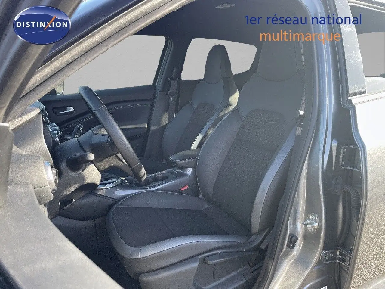 Intérieur avant droit du Nissan Juke gris squale métal 2024, sièges en cuir gris et tissu avec console centrale visible.
