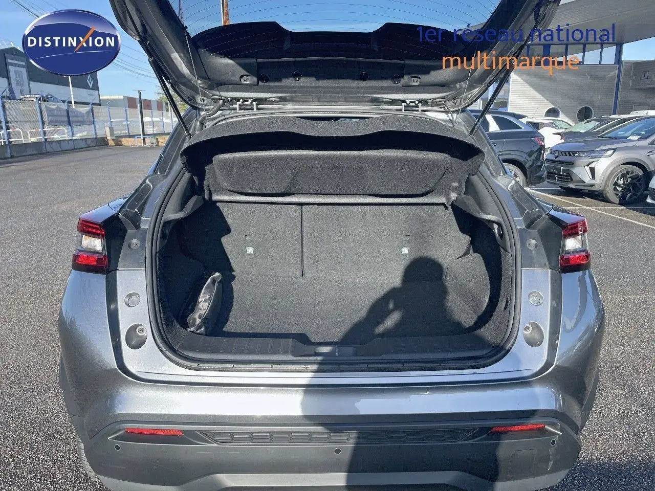 Coffre ouvert vu de l'arrière d'un Nissan Juke 2024 gris squale métal, montrant l'espace de chargement vide.