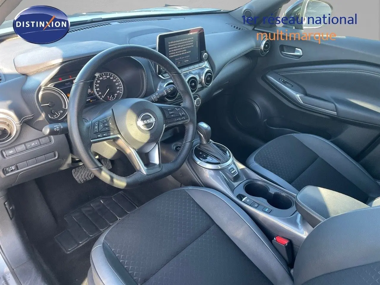 Vue intérieure avant du Nissan Juke 2024 avec volant multifonction, écran tactile et sellerie noire en tissu et cuir.