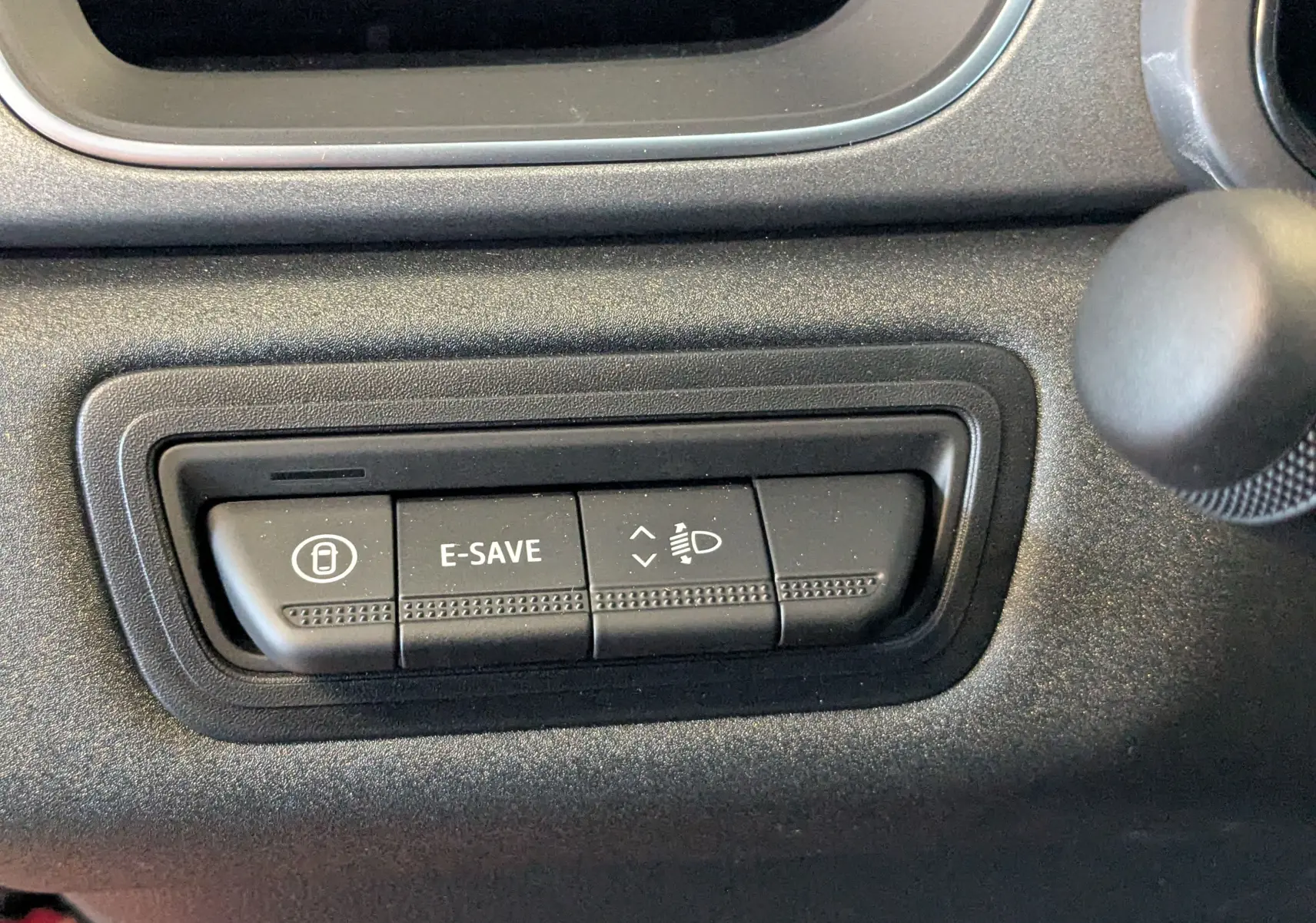 Gros plan sur les boutons de commande E-SAVE et réglage des phares dans l'habitacle du Renault Captur hybride 2025.