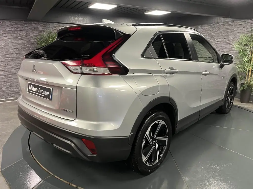Vue 3/4 arrière droite du Mitsubishi Eclipse Cross gris métallisé avec jantes alliage bi-ton et toit noir en intérieur showroom.