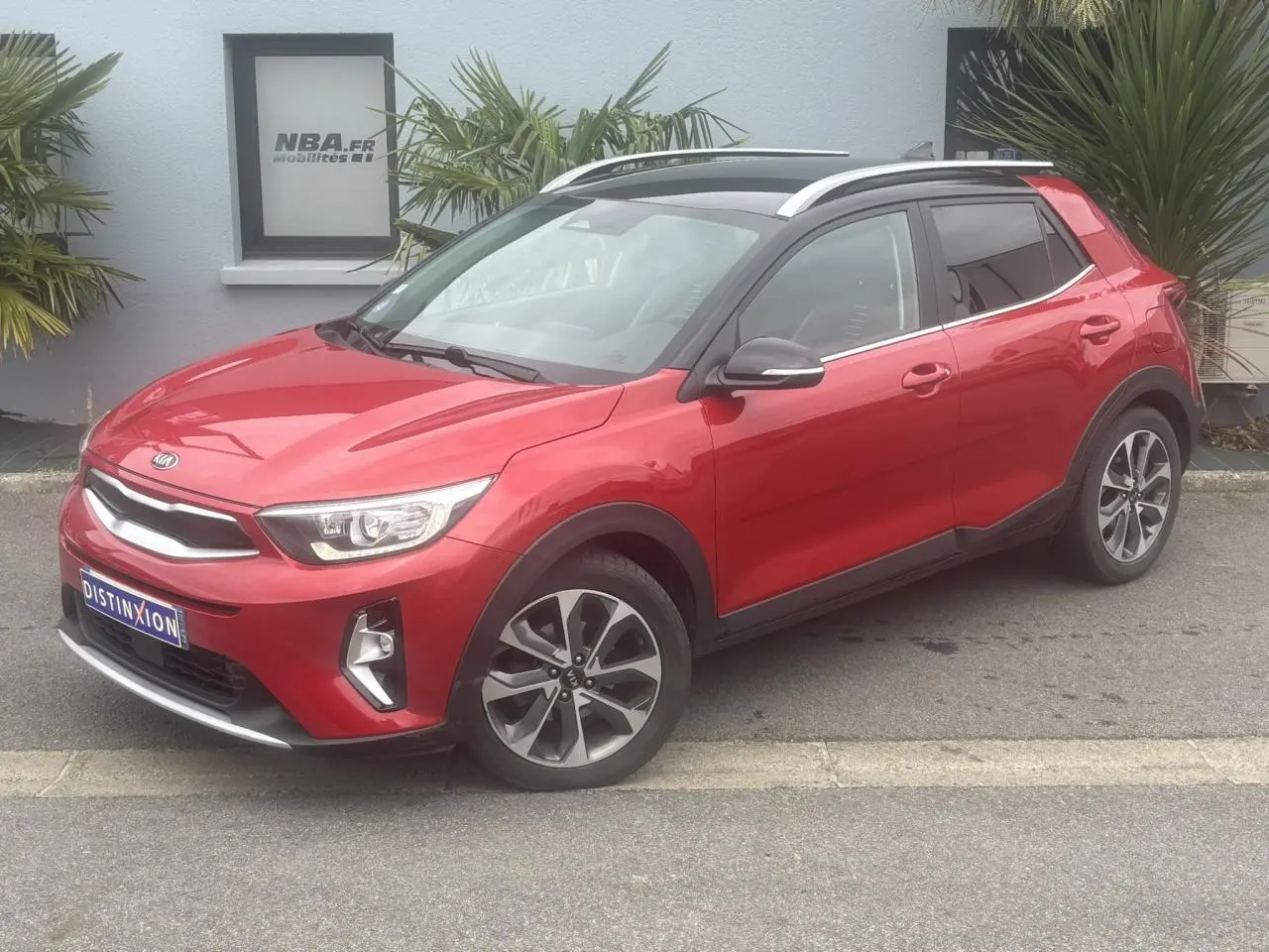 KIA Stonic rouge métallisé vue 3/4 avant droit avec jantes alliage et toit ouvrant panoramique.