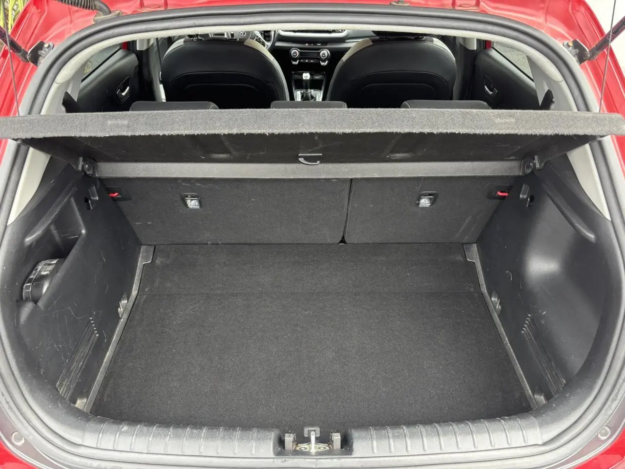 Coffre ouvert vu de l'arrière d'un KIA Stonic rouge, montrant l'espace de chargement et l'intérieur noir.