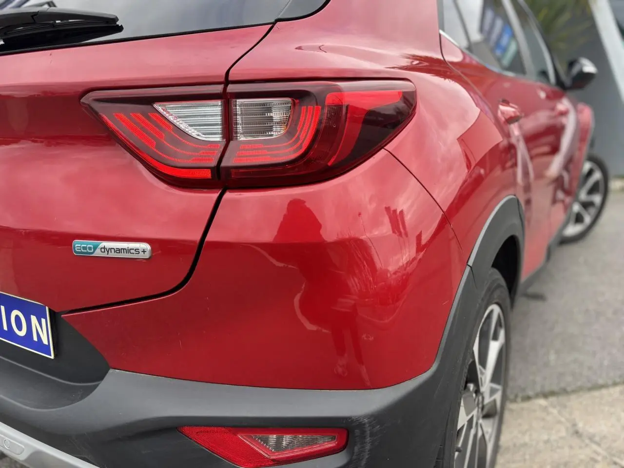 Vue 3/4 arrière droite d'un KIA Stonic rouge métallisé avec feux LED et badge eco dynamics+ visible.