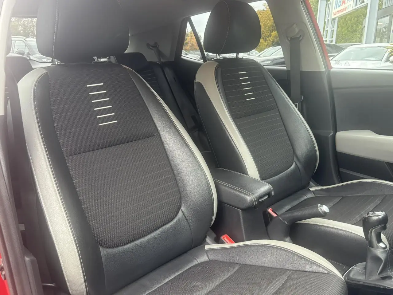 Vue intérieure des sièges avant noirs et gris du KIA Stonic rouge, avec levier de vitesse manuel visible.