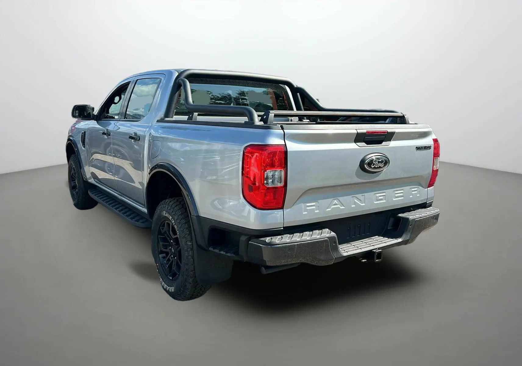 Vue 3/4 arrière droite du Ford Ranger gris iconic avec arceaux noirs et attelage visible sur fond neutre.