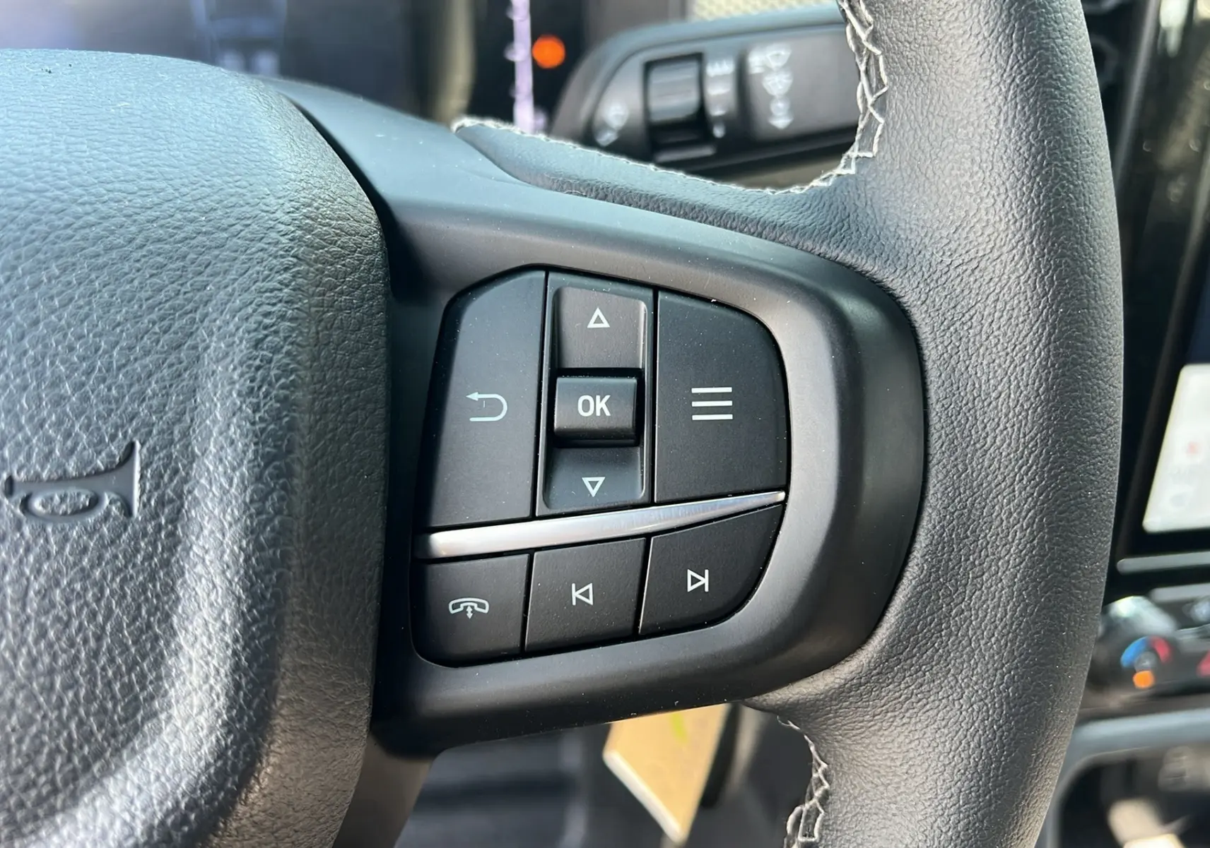 Gros plan sur les commandes multifonctions du volant cuir du Ford Ranger 2025 gris iconic, avec écran et climatisation en arrière-plan.