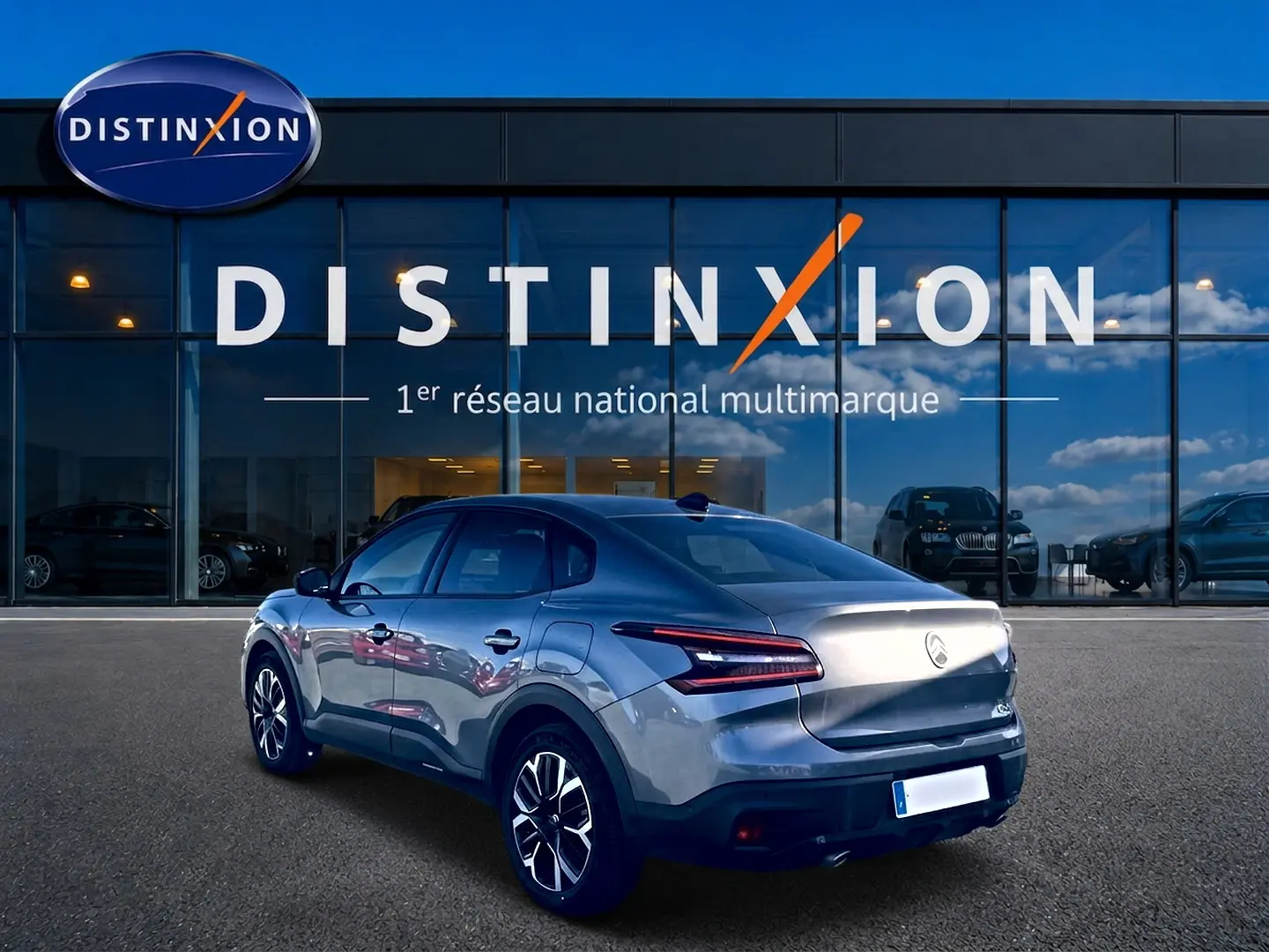 Vue 3/4 arrière droite d'une Citroën C4 X gris mercure, avec feux LED et jantes alu visibles devant un showroom Distinxion.