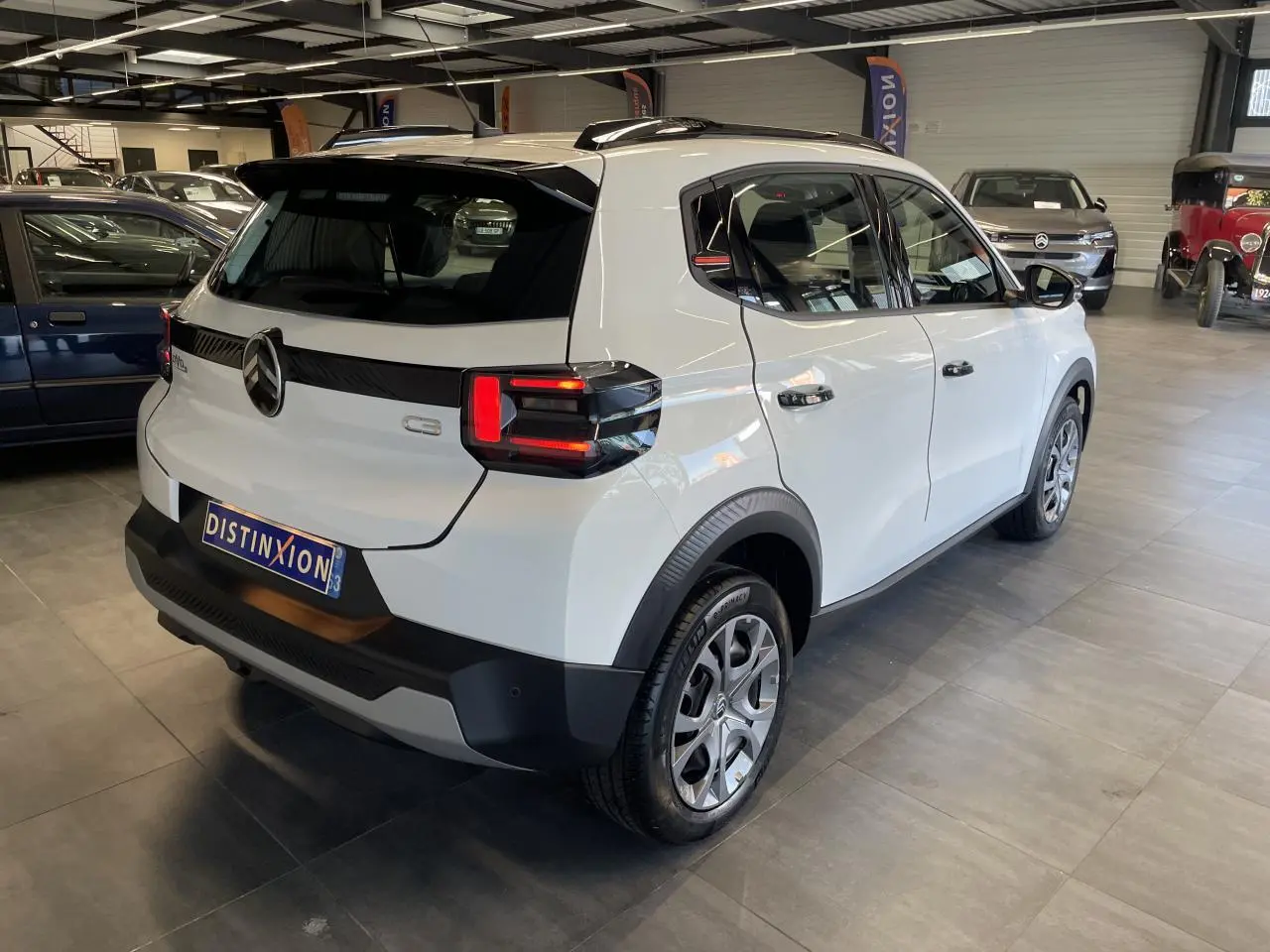 Vue 3/4 arrière droite d'une Citroën C3 blanche avec barres de toit noires et feux arrière LED distinctifs.