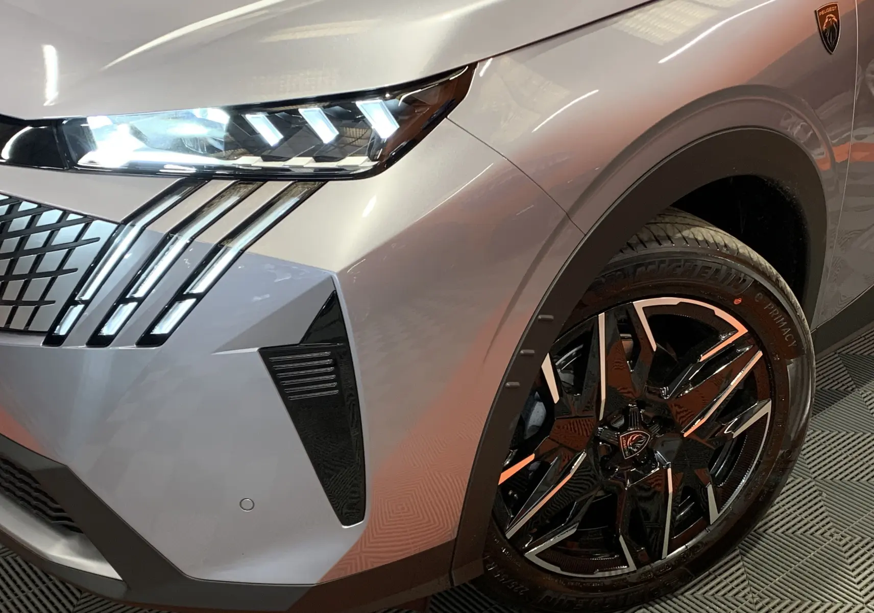 Gros plan sur l'avant droit gris Artense du Peugeot 3008 III GT Hybrid 136 avec phares LED et jante noire stylée.