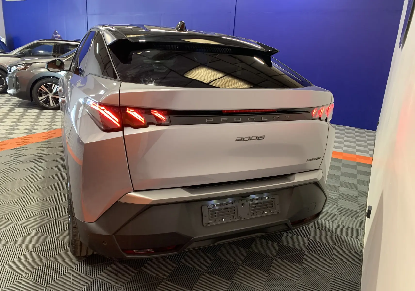 Vue arrière droite du Peugeot 3008 III GT Hybrid 136 e-DSC6 gris Artense avec feux LED allumés en intérieur showroom.