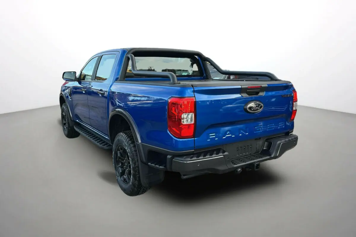 Vue 3/4 arrière du Ford Ranger bleu lightning avec arceaux noirs et attelage visible sur fond neutre.