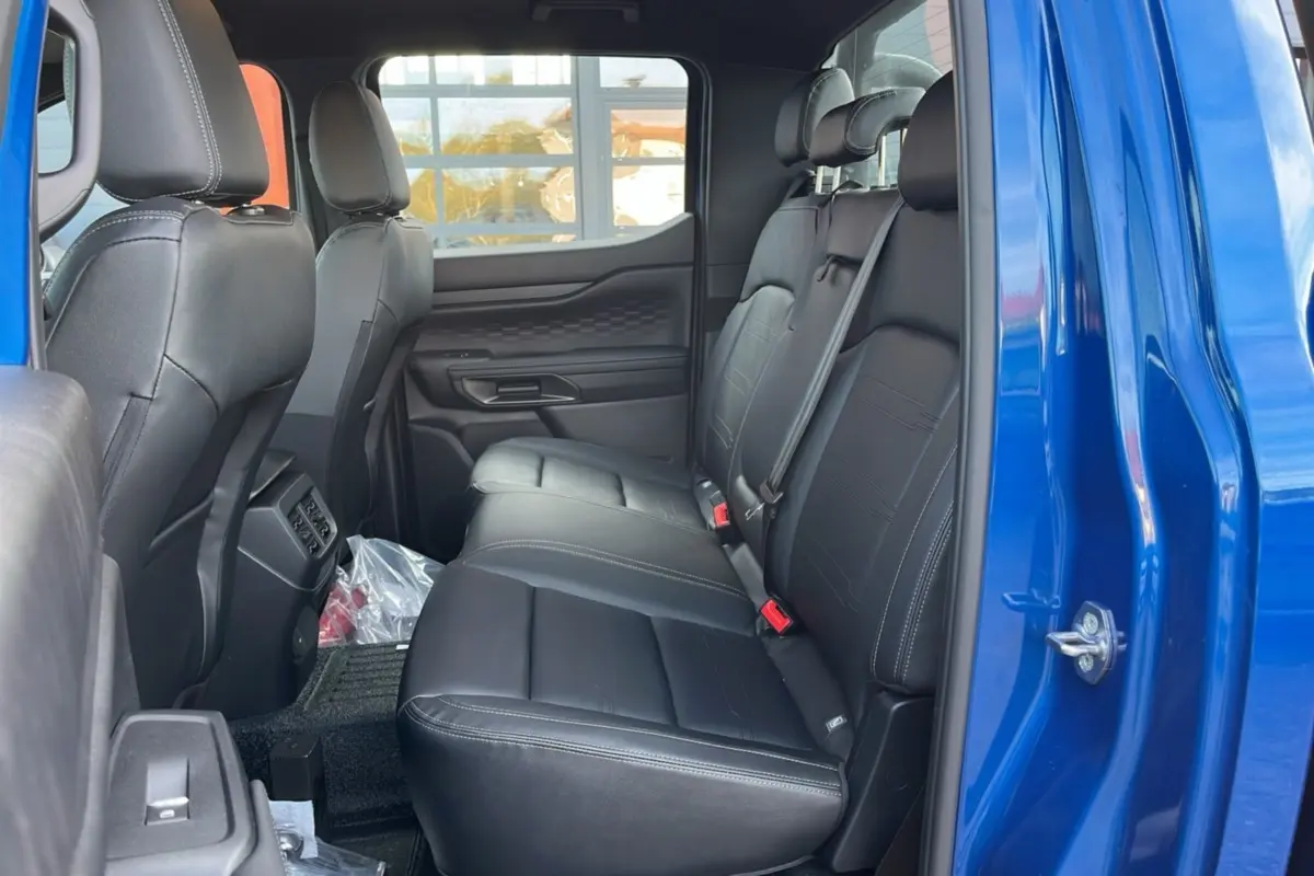 Vue côté droit de l'intérieur arrière du Ford Ranger 2025 bleu lightning avec sièges en cuir noir et ceintures de sécurité visibles.
