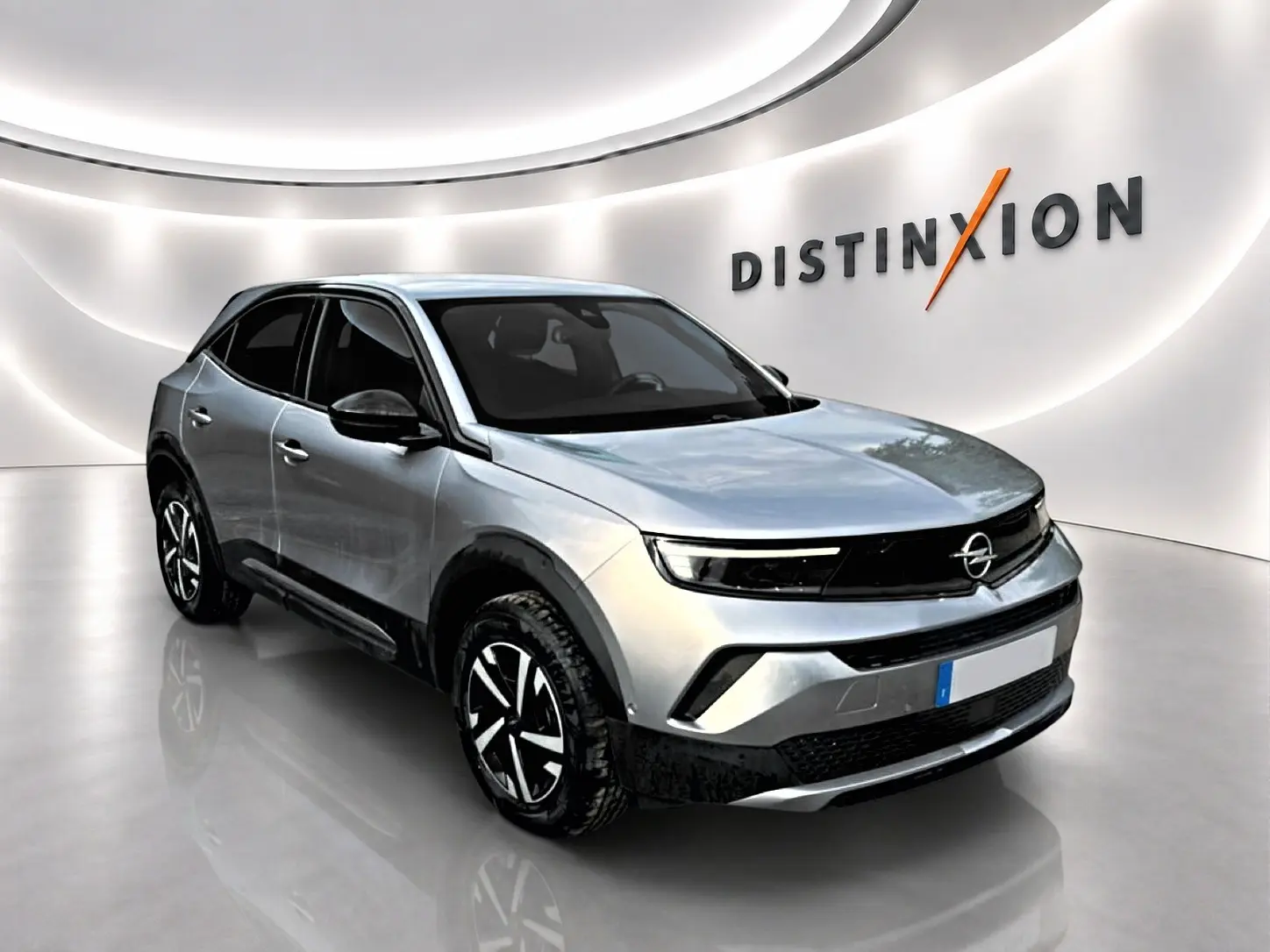 Opel Mokka gris en 3/4 avant droit, avec calandre noire et jantes au design moderne, dans un showroom lumineux.