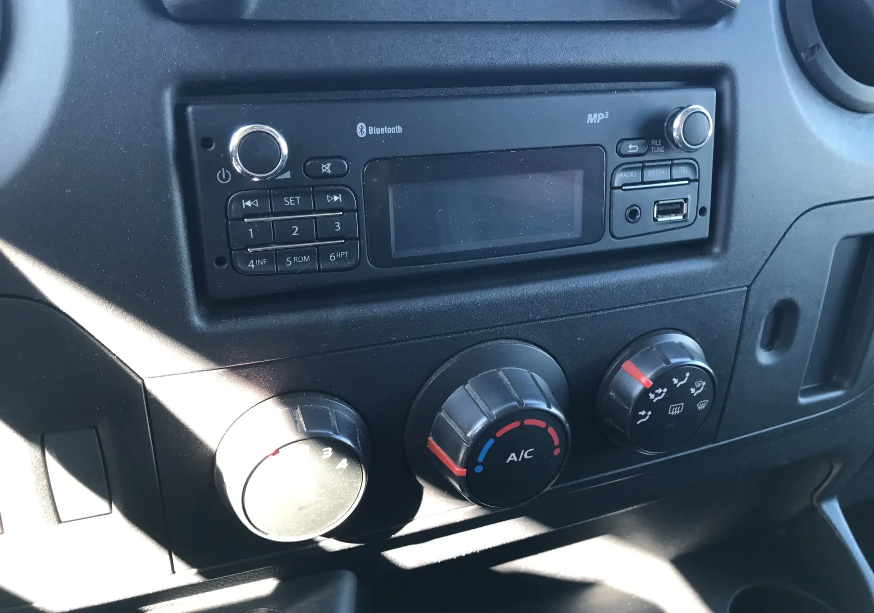 Gros plan sur la console centrale noire du Renault Master 2016, mettant en valeur la radio Bluetooth et les commandes de climatisation.