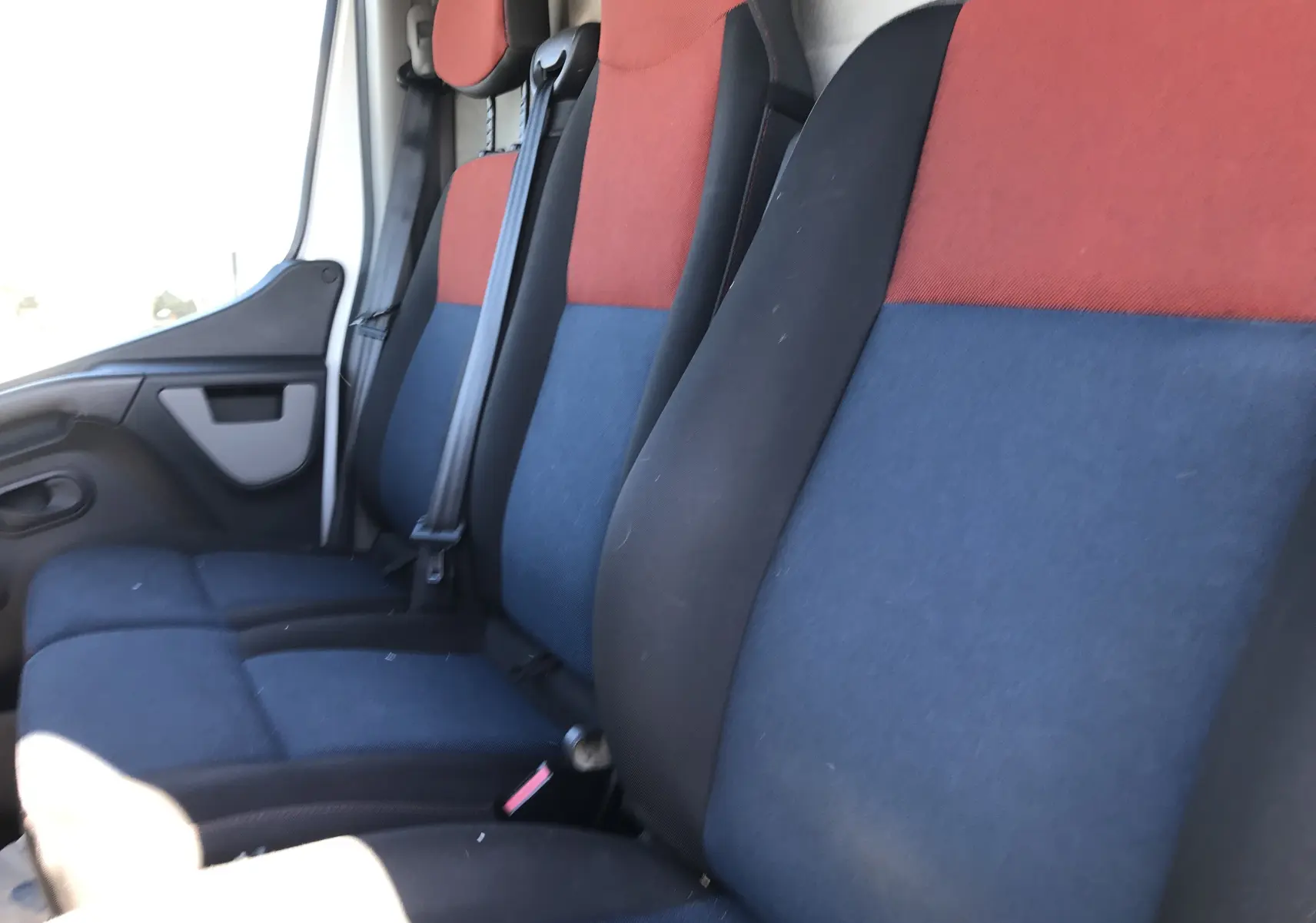 Vue intérieure des sièges avant du Renault Master 2016, tissu bicolore rouge et bleu avec ceintures de sécurité.