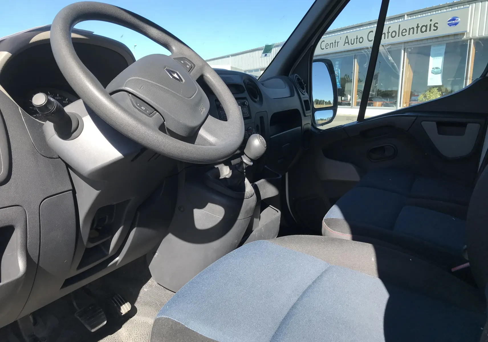 Vue intérieure côté conducteur du Renault Master blanc 2016, volant, tableau de bord et sièges en tissu bleu visibles.