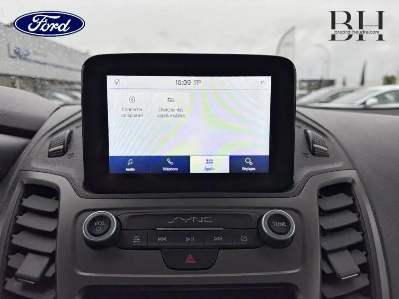 Vue rapprochée de l’écran tactile SYNC 3 du tableau de bord du Ford Transit Connect blanc glacier, avec commandes audio visibles.