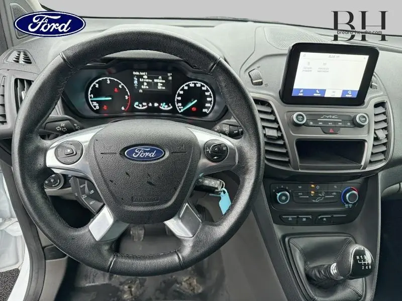 Vue intérieure centrée sur le volant multifonction noir et la console centrale avec écran tactile du Ford Transit Connect blanc glacier.