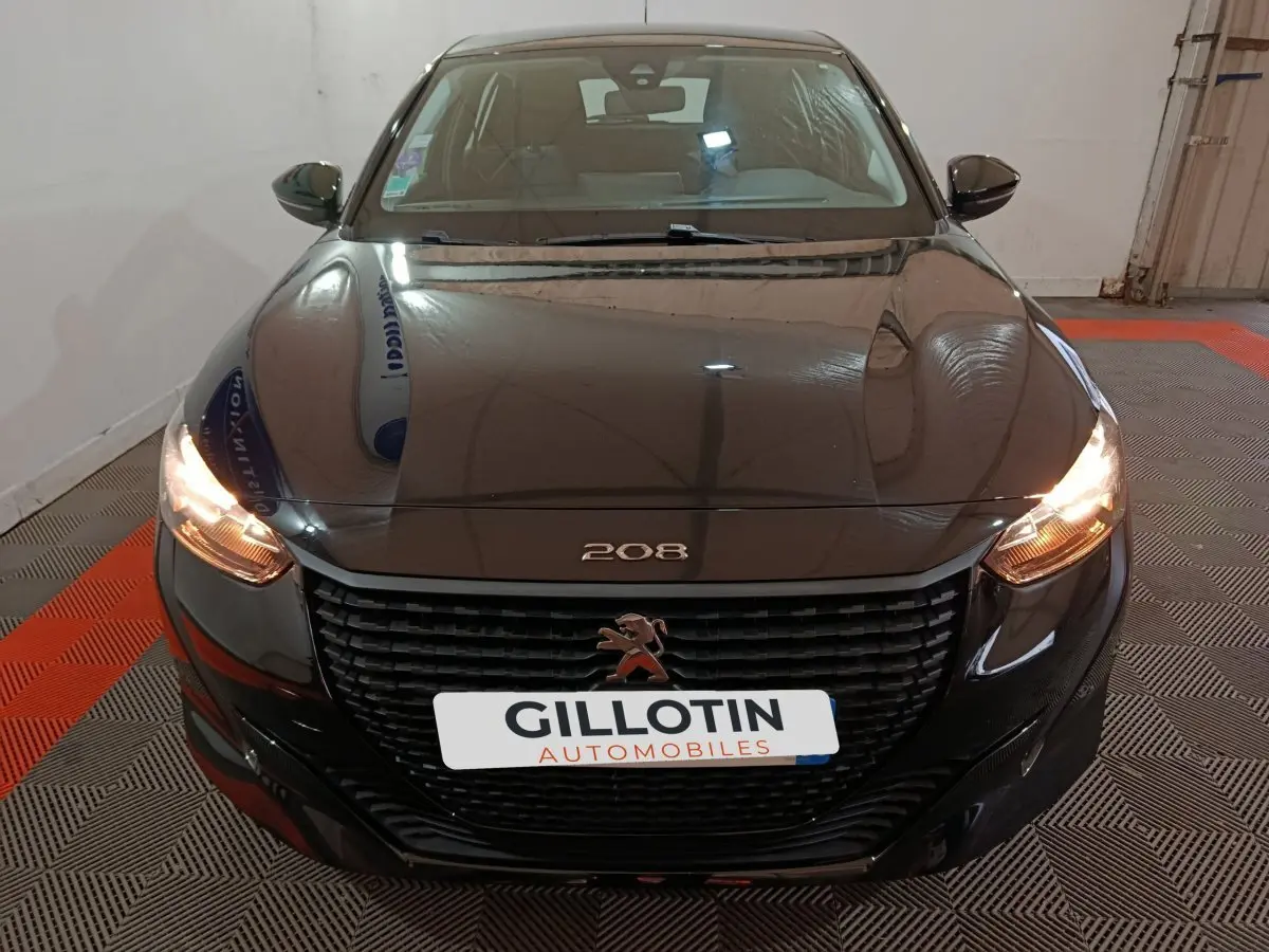 Vue avant d'une Peugeot 208 noire de 2022 avec phares allumés et calandre noire distinctive.