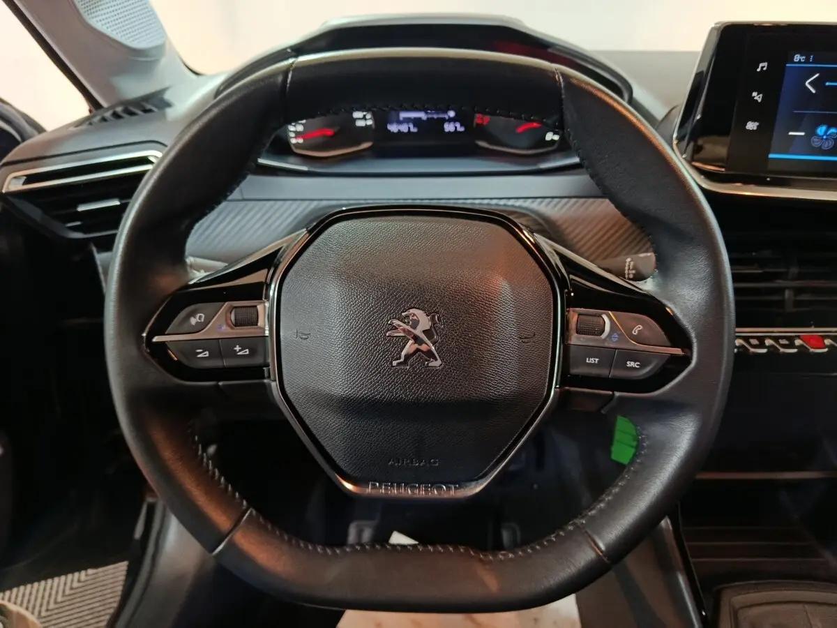 Vue rapprochée du volant noir de la Peugeot 208 2022 avec commandes intégrées et tableau de bord numérique en arrière-plan.