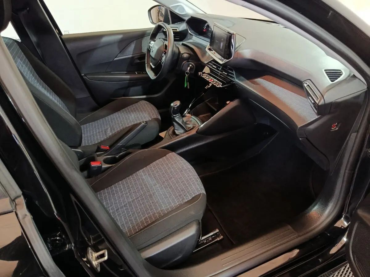 Intérieur avant droit de la Peugeot 208 noire, montrant sièges tissu, volant réglable et écran tactile central.