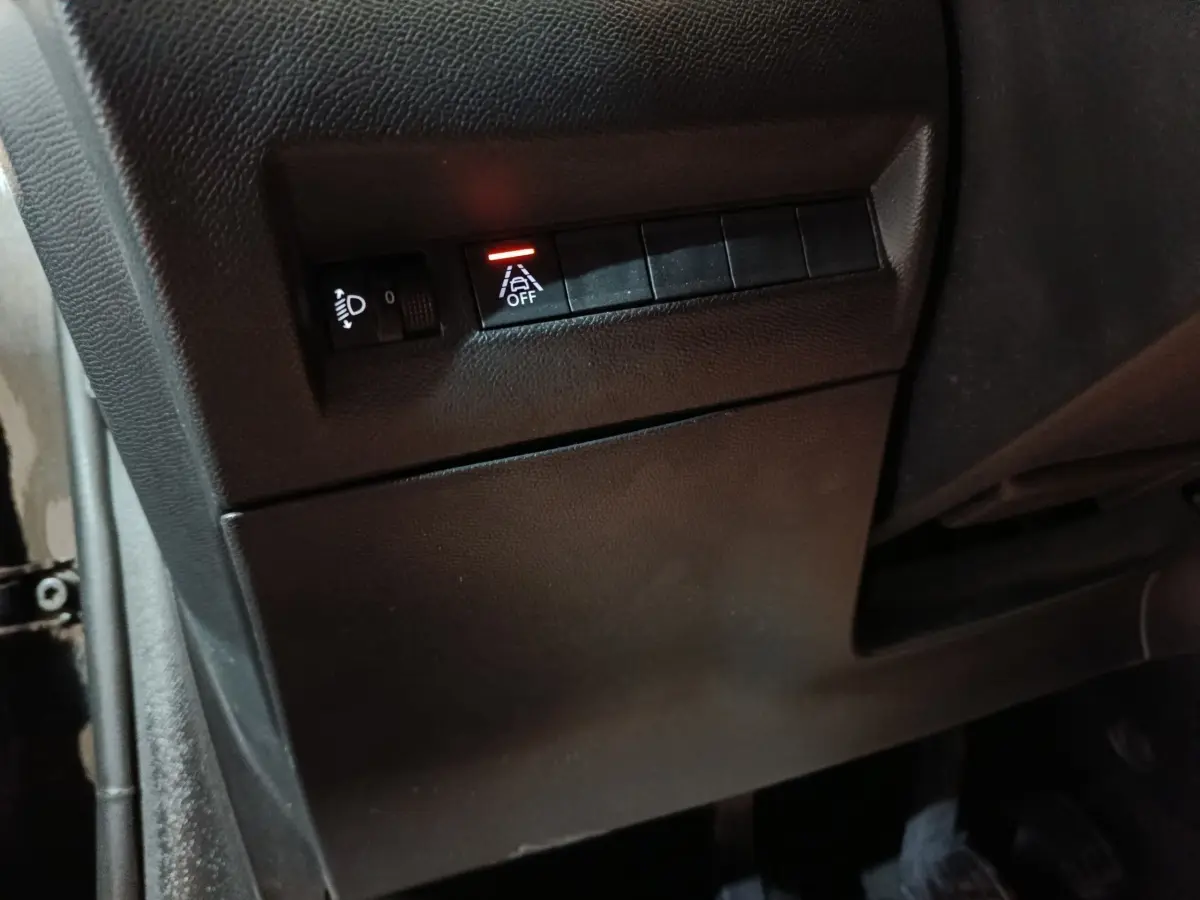 Détail intérieur côté gauche de la Peugeot 208 noire 2022 montrant les commandes de réglage des phares et d'assistance à la conduite.