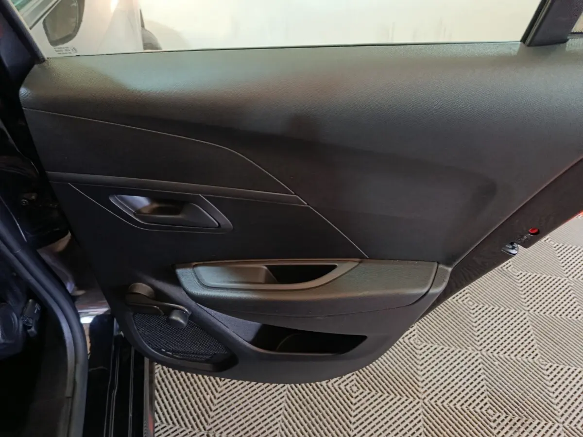 Vue intérieure de la porte arrière gauche noire d’une Peugeot 208 1.2 PT 75 S&S Premium 2022 avec poignée et haut-parleur intégrés.
