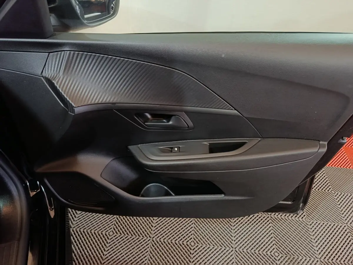 Vue intérieure côté gauche de la porte avant d'une Peugeot 208 noire avec insert décoratif effet carbone.