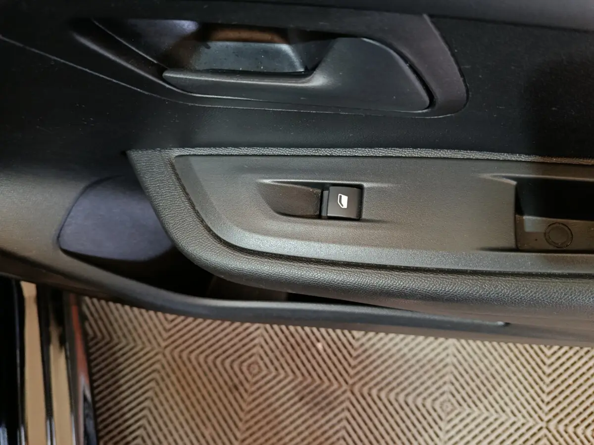 Gros plan sur la commande de lève-vitre côté conducteur de la Peugeot 208 noire, intérieur en plastique noir.