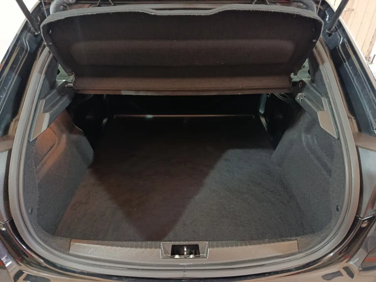Coffre ouvert vu de l'arrière d'une Peugeot 208 noire, montrant un espace de chargement vide et propre.