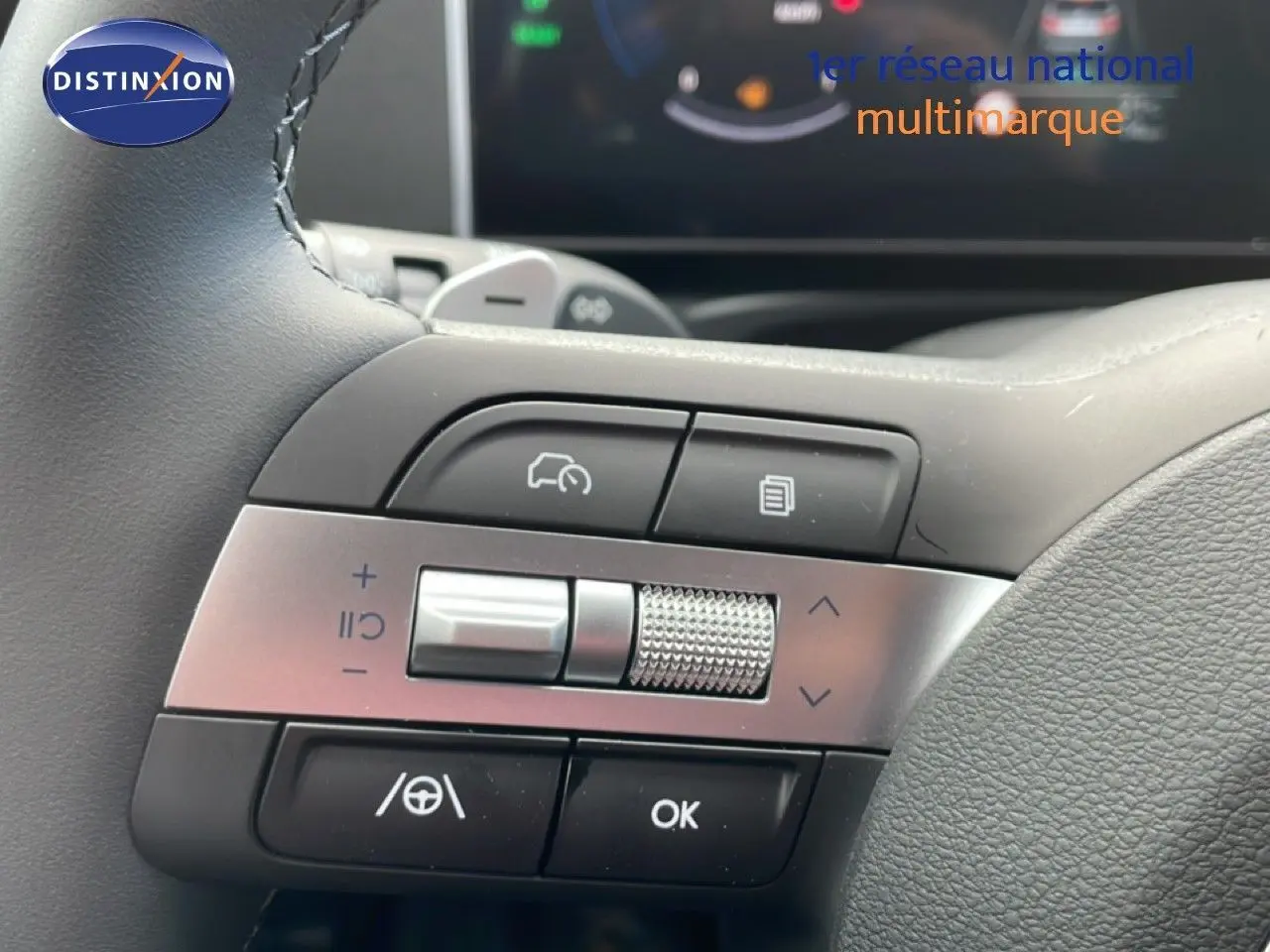 Gros plan sur les commandes multifonctions côté gauche du volant du Hyundai Tucson blanc Atlas 2026, avec molette métallique et boutons noirs.