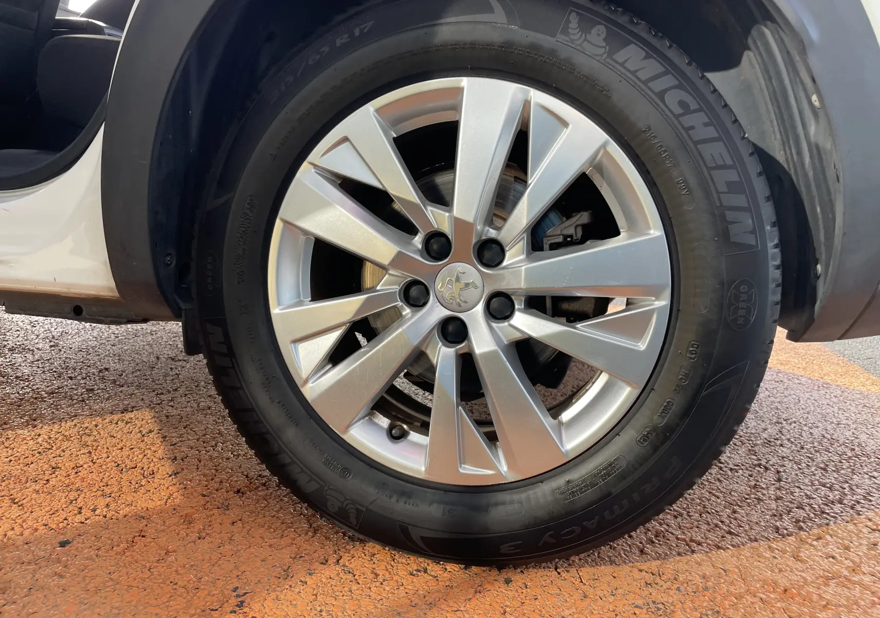 Gros plan sur la roue avant gauche d’un Peugeot 3008 blanc de 2018, jante alliage argentée et pneu Michelin visible.
