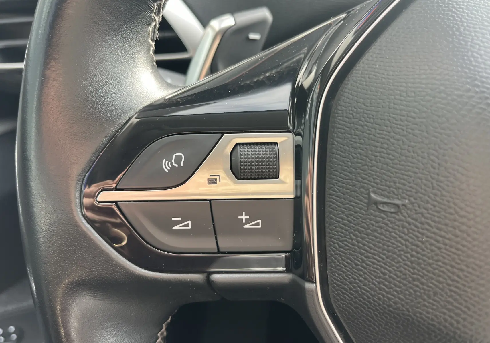 Gros plan sur les commandes gauche du volant noir du Peugeot 3008 blanc, avec boutons de volume et commande vocale.
