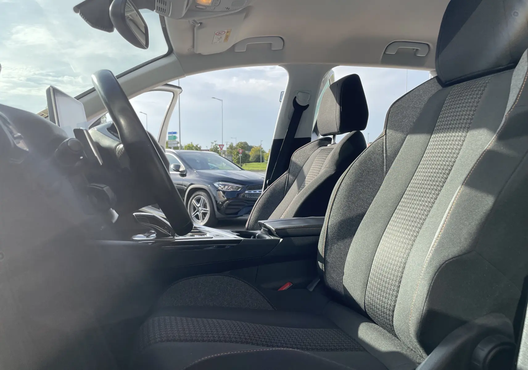 Intérieur avant du Peugeot 3008 2018 avec sièges gris-noir, volant multifonction et porte conducteur ouverte sur fond extérieur.