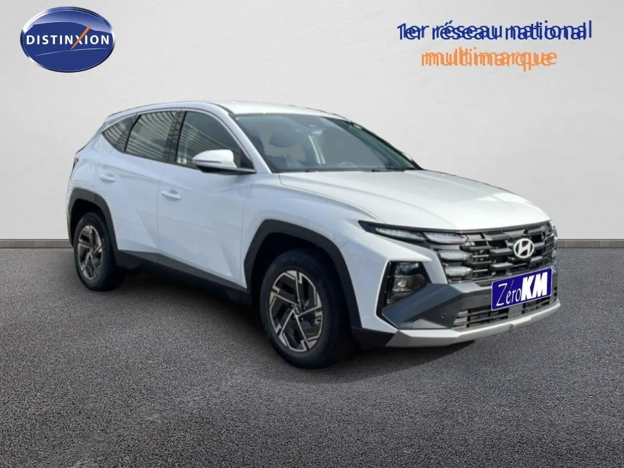 Hyundai Tucson blanc atlas en 3/4 avant droit, avec calandre distinctive et jantes bi-ton modernes.