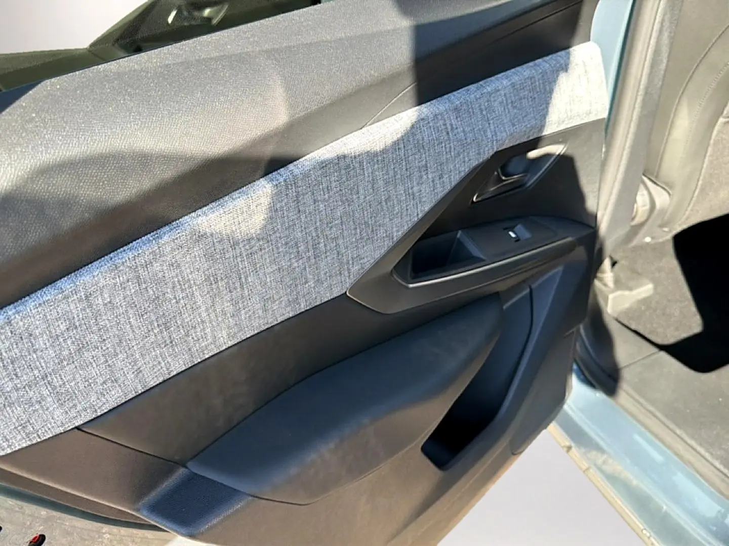 Vue intérieure côté gauche de la porte avant d’un Peugeot 3008 bleu Ingara avec habillage tissu gris et plastique noir.