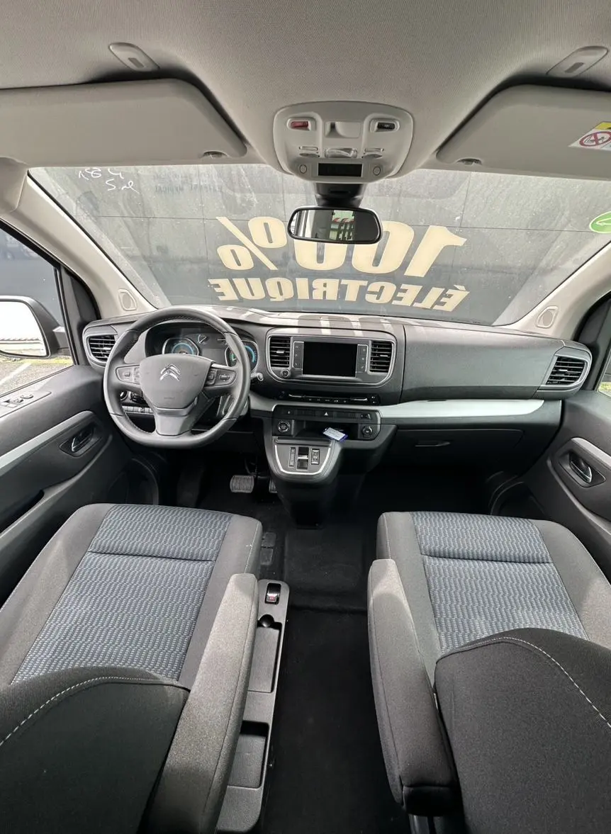 Vue intérieure frontale du Citroën Jumpy van électrique, montrant tableau de bord et sièges tissu noir avec volant multifonction.